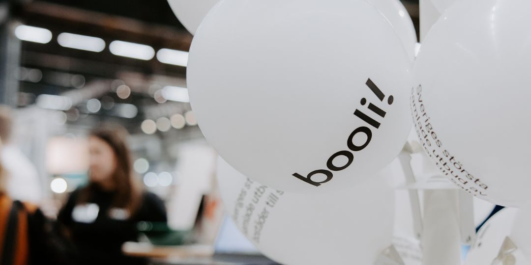 Booli_ballonger_1080x540px Bild på vita ballonger med svart text där det står booli! I bakgrunden skymtar en människa